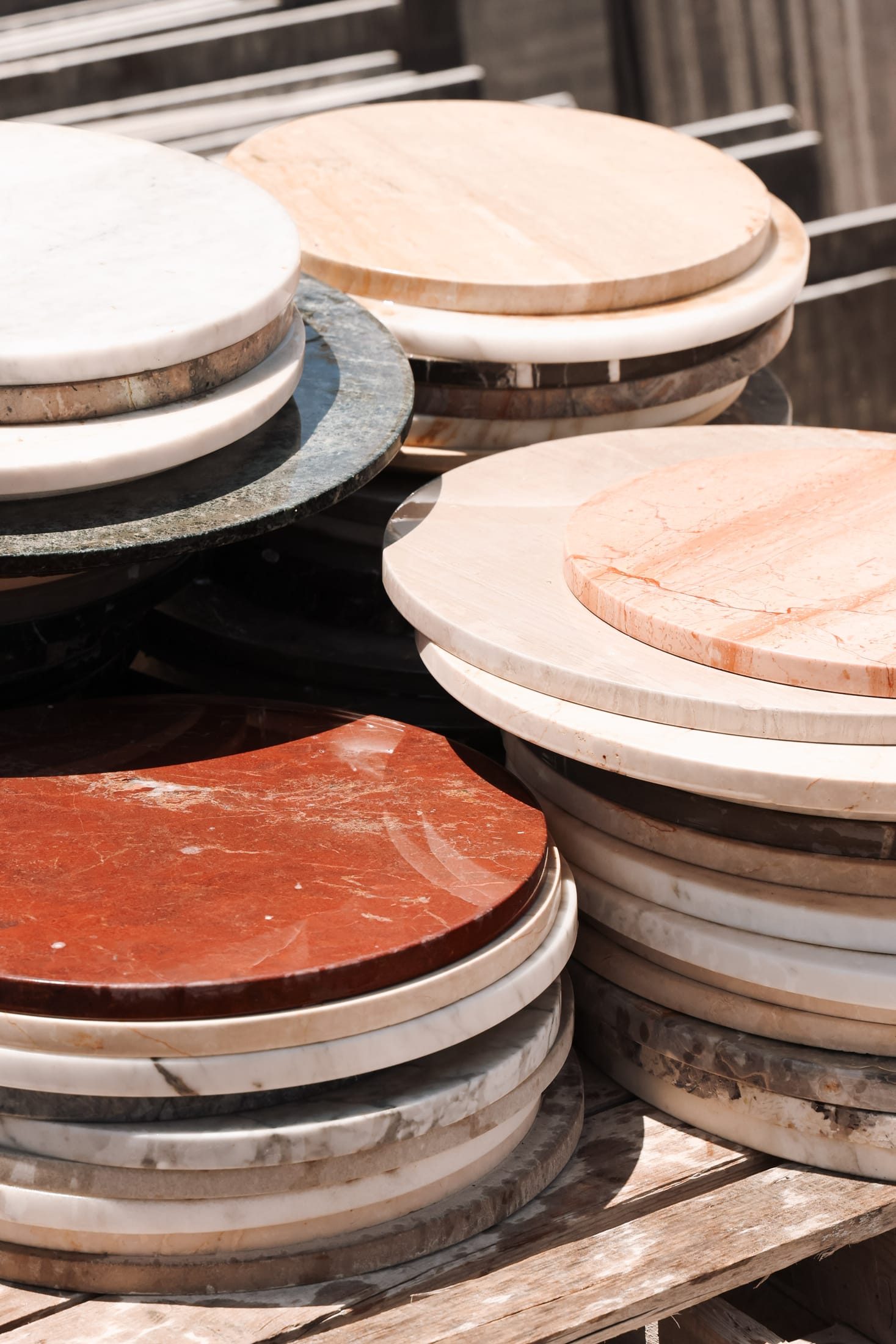 A stack of round stone tabletops — rosso, green, cream and travertine — at the Zein Group atelier