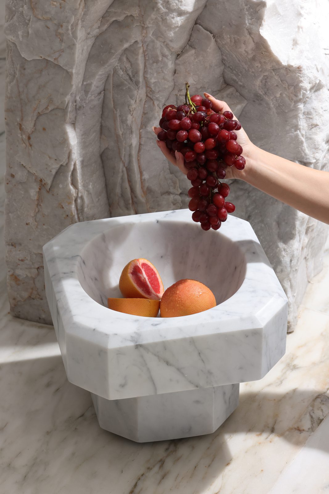 Hand placing grapes in a white marble fruit bowl