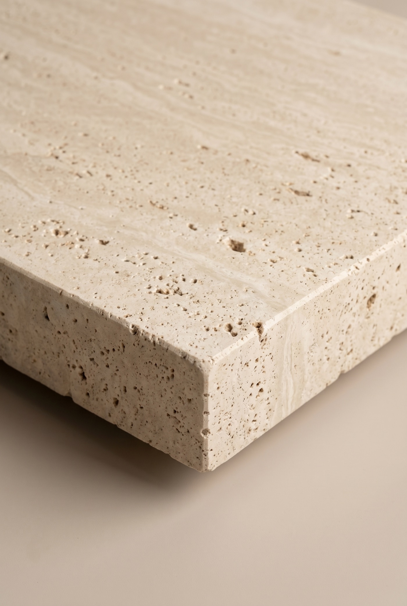 Honed travertine block with a clean cut edge profile and natural open pores, photographed in soft studio light